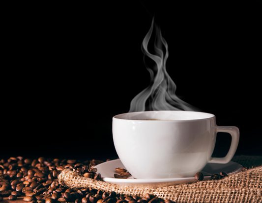 steaming hot coffee with the mug sat on a small plate surrounded by coffee beans